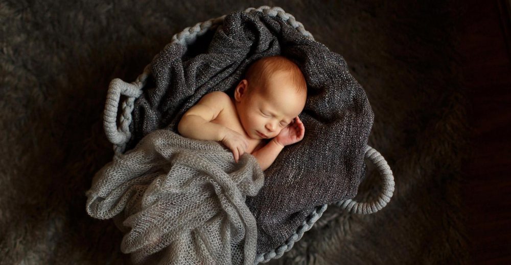 newborn girl snuggled up in grey basket